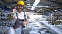 portrait of factory worker in protective equipment holding thumbs up in production hall