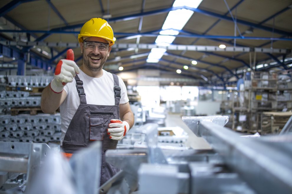 portrait of factory worker in protective equipment holding thumbs up in production hall